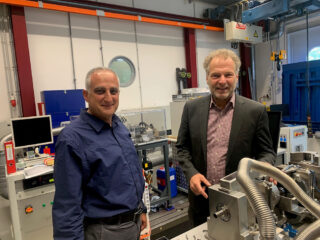 Prof. Ashhab und Prof. Wartzack stehen vor einer Maschine in einem Raum des Lehrstuhl für Konstruktionstechnik.