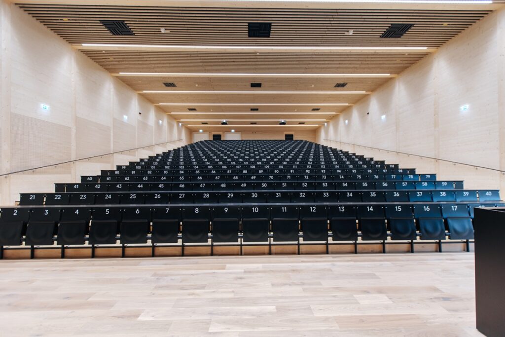 Ein großer leerer Hörsaal mit schwarzen Sitzen und Wänden aus hellem Holz.