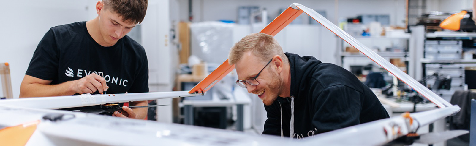 Zwei Männer in schwarzen T-Shirts arbeiten gemeinsam an einer Drohne.