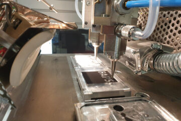 Ein Aerosol-Jet-Drucker druckt auf eine dunkle Platte den Schriftzug FAPS.